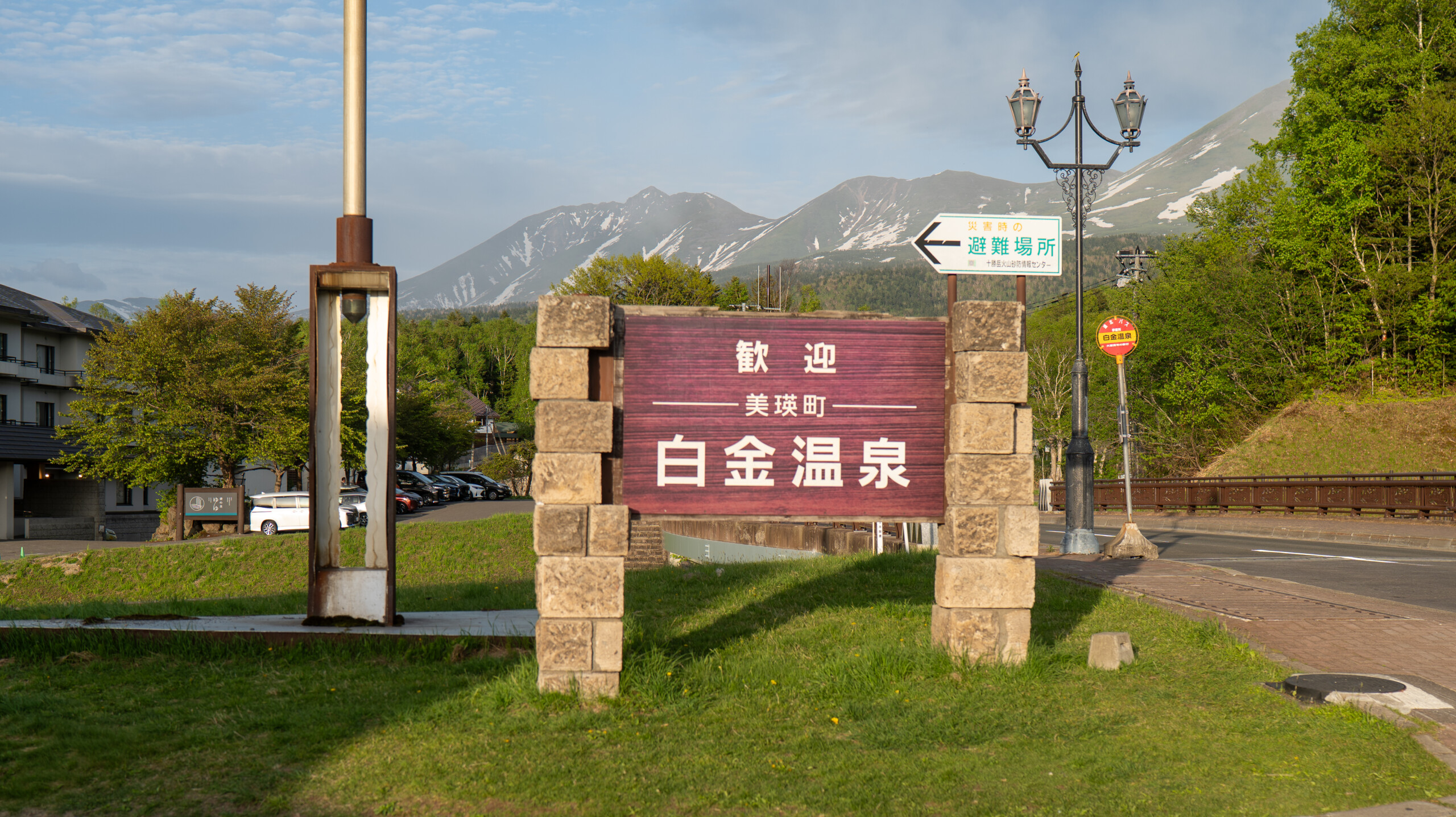 美瑛町白金温泉の入口看板。背後に十勝岳連峰と白金温泉街の風景が広がる